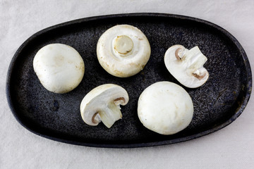 White closecup whole and cut half mushrooms on rustic cast iron plate