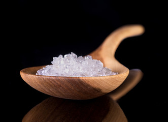 Wooden spoon on dark background with reflection on table surface.