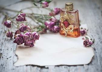 Dry tea roses and vintage perfume bottle on the old paper