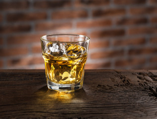 Whiskey glass or glass of whiskey with ice cubes on the wooden background.