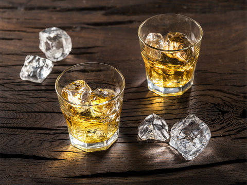 Whiskey glasses or glasses of whiskey with ice cubes on the wooden table.