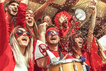 group of fans dressed in red color watching a sports event - obrazy, fototapety, plakaty