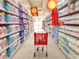 Supermarket aisle with full red white shopping cart trolley