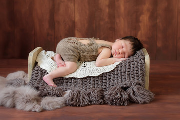 Portrait of a newborn baby boy. He is sleeping on a miniature wooden bed. Shot in the studio on a rustic wood background.