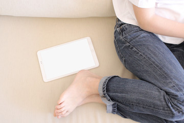 A teenage boy on a sofa, without socks and with an electronic tablet beside him.