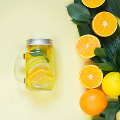 Summer refreshing cocktail with lemon, orange, mint and ice in mason jar on yellow. Tropical concept.