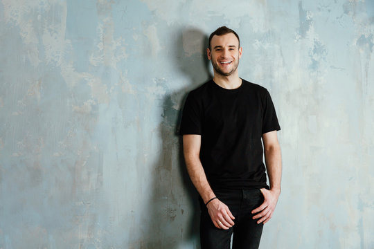portrait of a young man in a black T-shirt leaned against a vintage gray wall. Copy space.