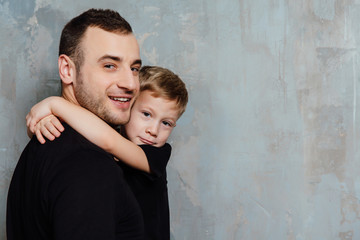 Obraz na płótnie Canvas Father and son embracing son on gray wall background. Fashion man and boy in black clothes.