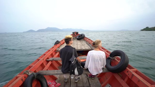 Camera rises from inside the boat to above the boat and reveals a couple sitting, traveling to an island in front of them.