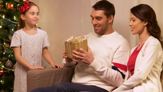 holidays, family and celebration concept - happy mother, father and little daughter with christmas present at home