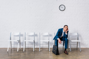 Bored man with briefcase sitting on chair and waiting