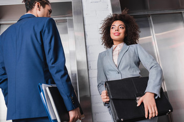 African American businesswoman with briefcase and man with folders waiting by elevator