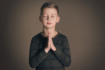 Religious little boy praying on dark background