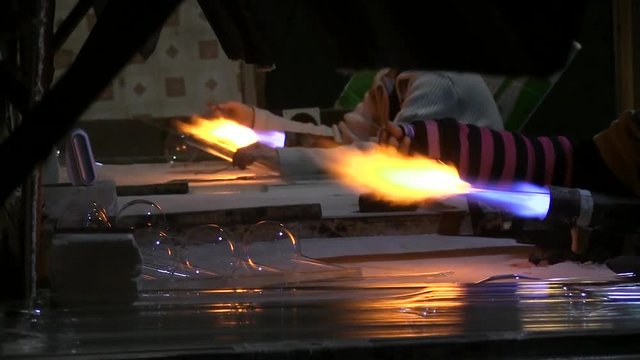 Glass blower forming beautiful piece of glass. Glassblowing Professional Working on Torch Flame with Glass Tubes. A glass crafter is burning and blowing an art piece