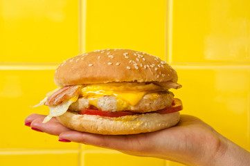 Chiken burger with shrimps holding in young woman hand on yellow