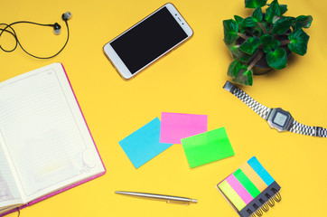 working space with a notebook, pen, clock, telephone, headphones on a yellow background. place for text. The working space of a freelancer, journalist, writer. On a bright yellow background. Top view.
