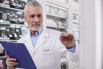 Naklejka na ściany i meble Medication list. Senior handsome male pharmacist stretching hand while using clipboard