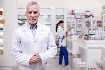 Welcome atmosphere. Mature vigorous male pharmacist posing on blurred background while looking at camera