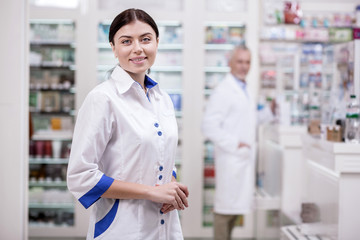 Qualified professional. Glad female pharmacist wearing uniform while smiling to camera