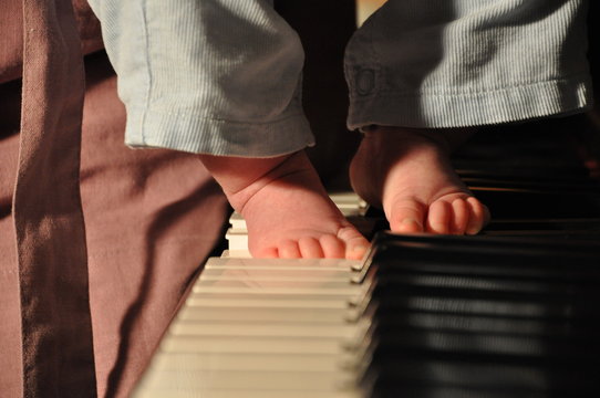 Closeup view on male babyboy bare feet with small toes playing on piano forte key board musical instrument with warm light indoor