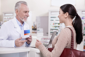 Obraz premium What you need. Senior joyful male pharmacist carrying drug while talking to client