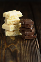 Block of white and dark chocolate pieces on wooden dark background in moodle style