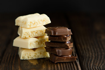 Block of white and dark chocolate pieces on wooden dark background in moodle style