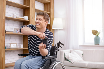 Happy weekends. Positive delighted brunette man sitting on his wheelchair and holding console