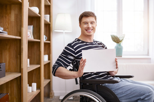 Emotional man. Smiling disabled male sitting on wheelchair and looking straight at camera
