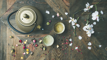 Traditional Asian tea ceremony arrangement. Flat-lay of iron teapot, cups, dried rose buds and blooming almond tree flowers over wooden table background, top view