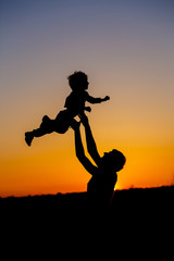 Fototapeta na wymiar Loving father and his little son having fan together outdoors. Happy family. Fatherhood. Toddler boy and his dad playing. Family as silhouette on sunset. Vertical photo