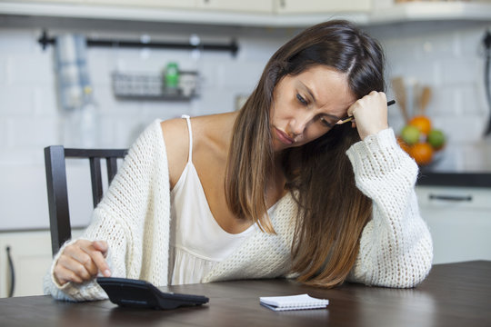 Worried woman sitting with bills and calculator in the kitchen at home