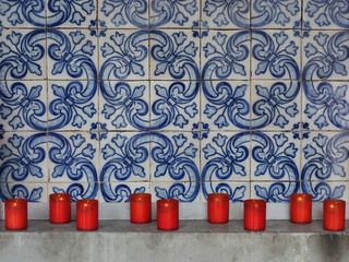 Red firing candles in catholic church on a background of Portuguese tiles.