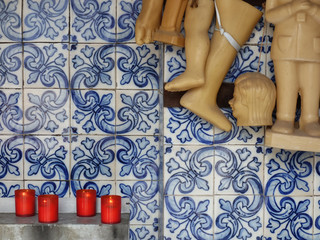 Wax votives (head, foot, leg, hand, child, baby) in catholic church on a background of Portuguese tiles.