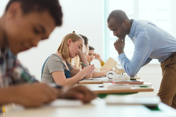Side view of multicultural writing schoolchildren and african american teacher checking