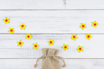 Sackcloth bag decorate with yellow paper flowers on white wood with copy space