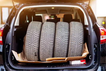 Stack of four used tires fitting perfectly in a blue cars trunk.