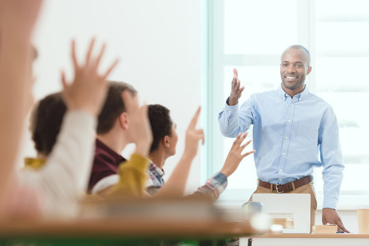 Smiling African American Teacher And Schoolchildren With Arms Up In Classroom