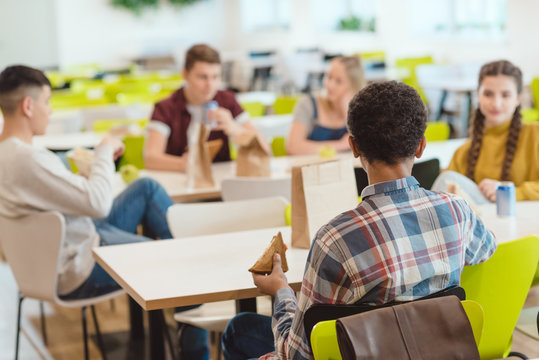 group of teen students chatting while taking lunch at school cafeteria