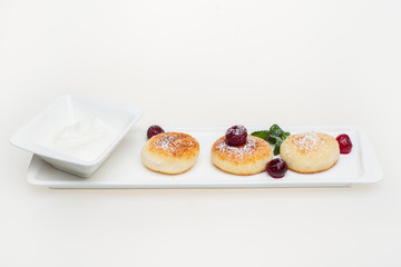 Cottage cheese pancakes with sour cream and berries on white plate