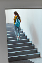 rear view of schoolgirl with backpack walking upstairs