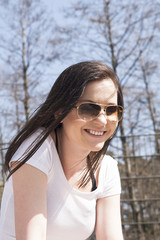 Beautiful young girl with long dark raven hair wearing sunglasses smiling honestly while being in the park at sunny day