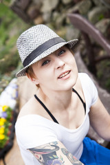 Natural looking woman with blonde short hair and tattoo, wearing nice hat, being in the garden