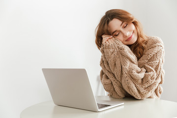Naklejka premium Image of relaxed woman 20s with closed eyes sitting at table in cafe, and using laptop
