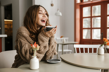 Picture in profile of happy smiling woman with brown curly hair, resting in cafe and drinking cup of tea or coffee