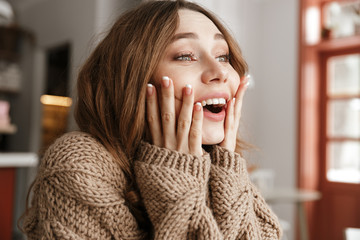 Portrait closeup of astonished woman in knitted sweater, sitting at table in coffee shop and...