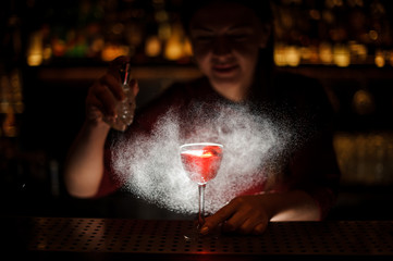 Barman decorating a glass of alcoholic cocktail with sparay