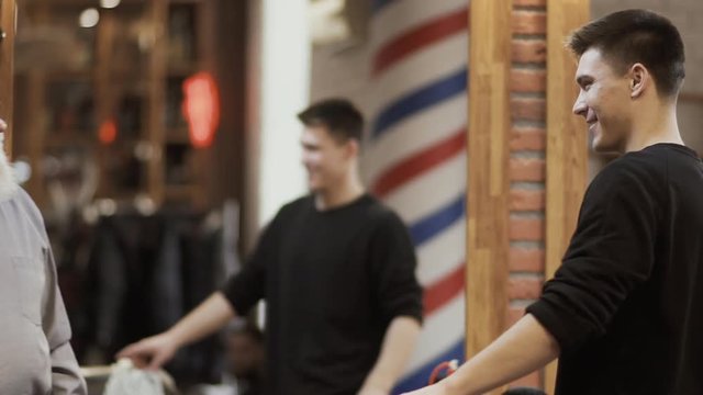 Happy mature man shakes hands with barber and thanks him for work