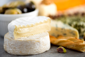 Assortment of hard, semi-soft and soft cheeses with olives, grissini bread sticks, capers, grape, on grey concrete backgound. Top view, copy space, flat lay. Cheese selection appetizer plate.