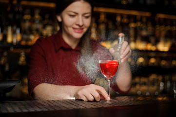 Bartender girl decorating a glass of alcoholic cocktail with sparay